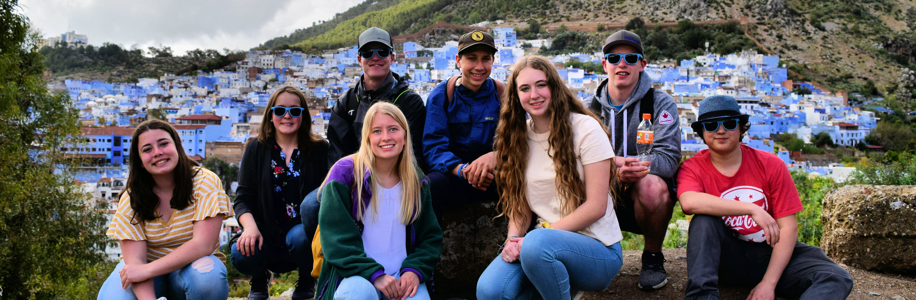 Eight fearless climbers perched upon a high mountain top with hundreds of blue houses in the valley below