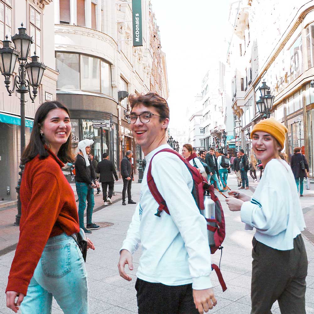 three young students prance through a busy city street