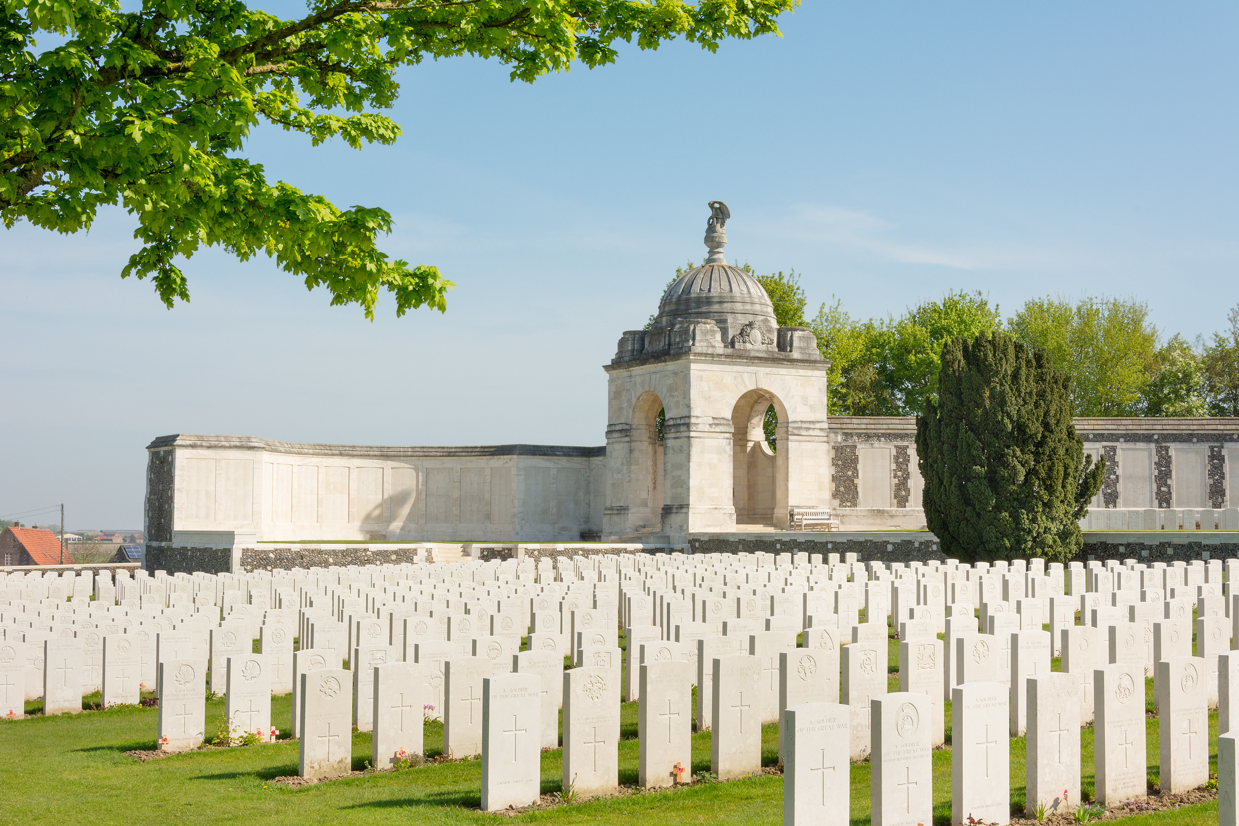 Rows of white headstones stretch across the Canadian Cemetery No. 2 at Vimy, France, under a clear blue sky. A domed memorial structure stands in the background.